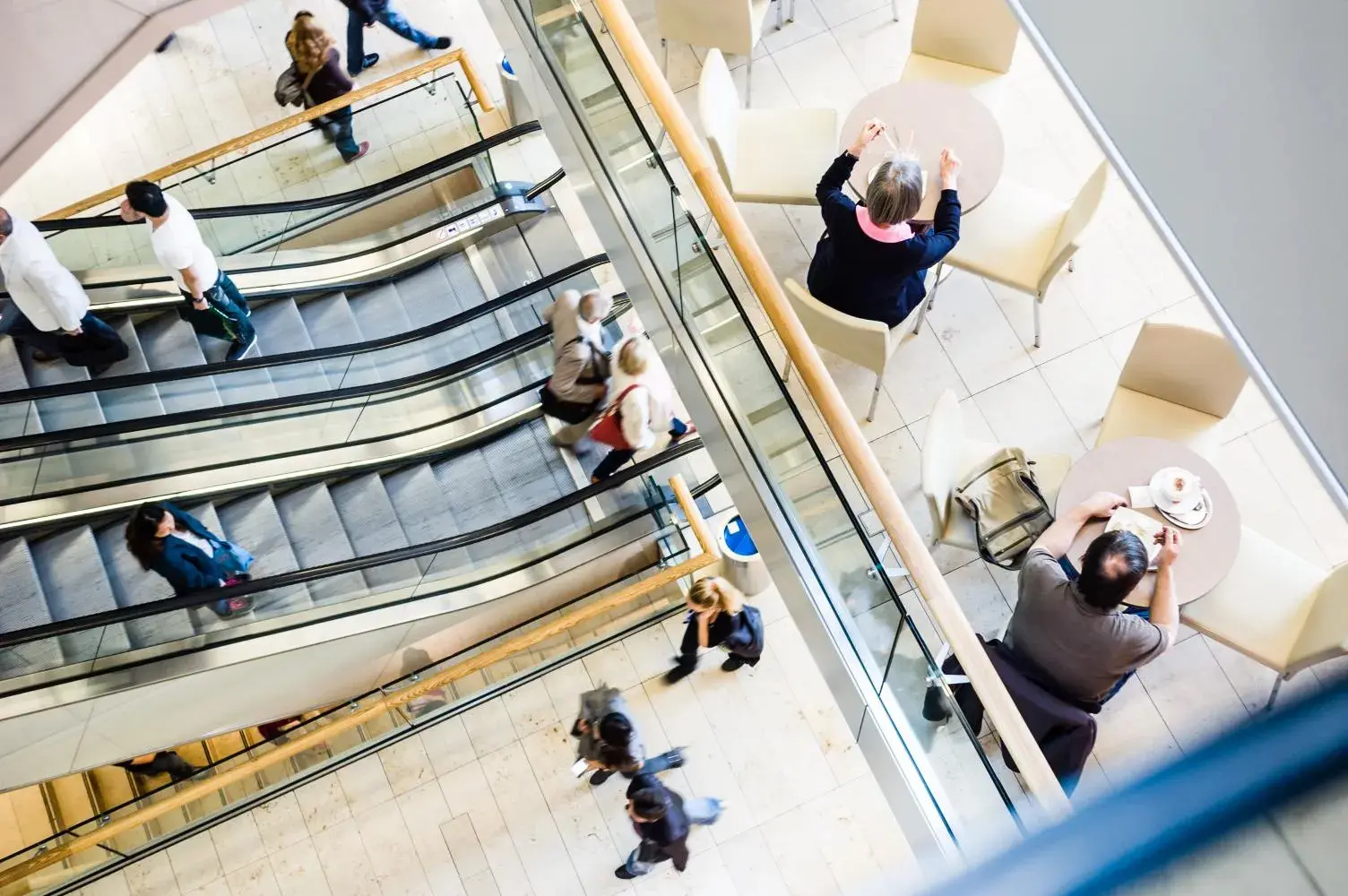 A birds eye view of a shopping centre, there are two escalators with people on them and a first floor retail mezzanine area in view.