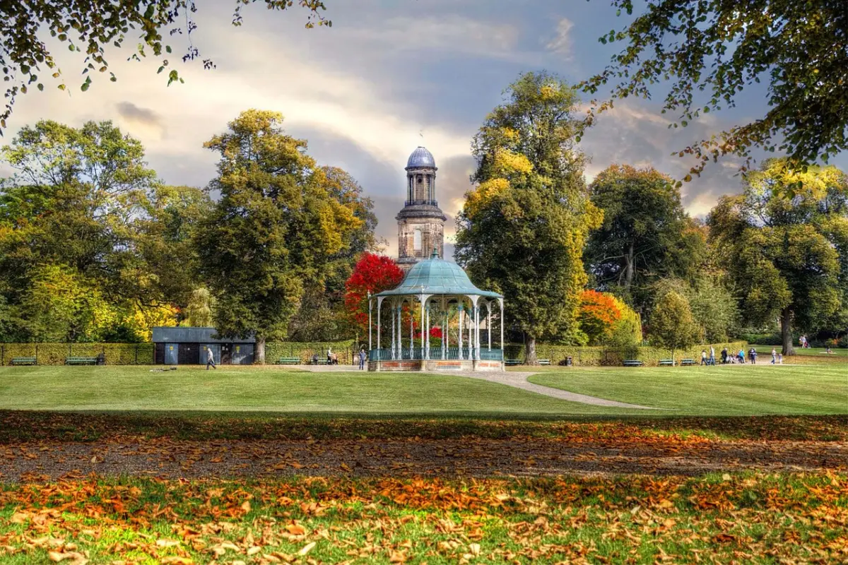 A country park in Shrewsbury, there is a covered seating area and a belltower in the distance.