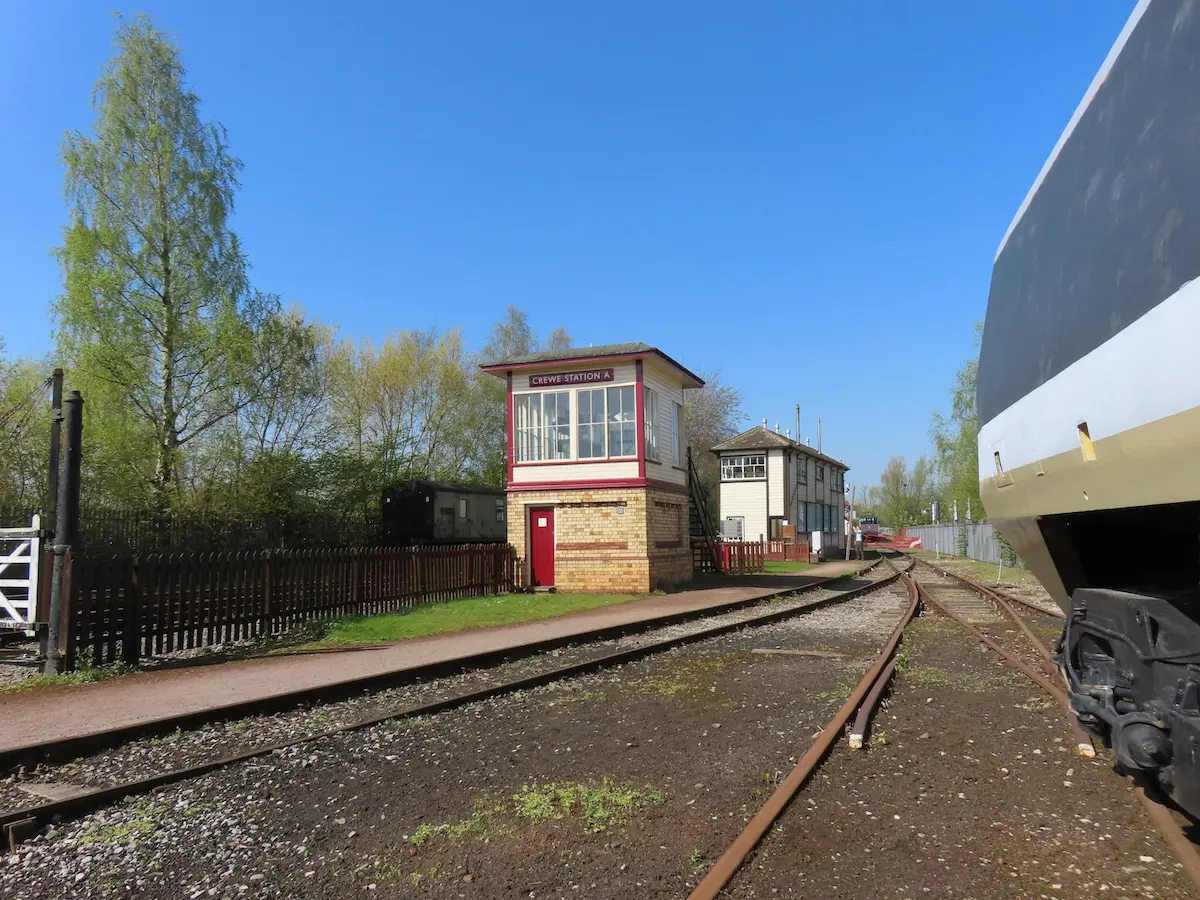 A ground level view of a small Crewe train station building from the tracks.